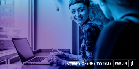 Auf dem Bild sieht man eine Frau mit kurzen Haaren, die eine andere Person anschaut und dabei lächelt. Sie sitzt vor ihrem Laptop und ist tätowiert. Das Bild ist mit einem blau-lila farbenden Flair überzogen.