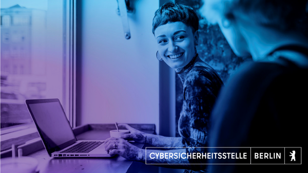 Auf dem Bild sieht man eine Frau mit kurzen Haaren, die eine andere Person anschaut und dabei lächelt. Sie sitzt vor ihrem Laptop und ist tätowiert. Das Bild ist mit einem blau-lila farbenden Flair überzogen.