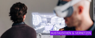 Auf dem Bild sieht man einen Mann mit einer Glatze und einer VR-Brille auf den Augen. Im Hintergrund ist eine Projektion sowie eine Person zu erkennen, die nach vorne zu der Projektion schaut.